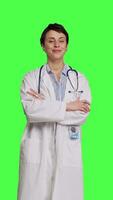 Front view Portrait of successful physician standing with arms crossed against greenscreen backdrop, wearing a white coat and stethoscope. Doctor feeling confident with healthcare expertise. Camera B. video