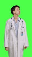 Front view Woman physician looking around for patients to come at checkup exams, waiting for someone standing against greenscreen backdrop. General practitioner with white coat feeling impatient. Camera B. video