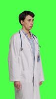 Side view Physician saying no and showing negative reaction symbol in studio, wearing a white coat and standing against greenscreen backdrop. Woman medic feeling displeased, rejection sign. Camera B. video