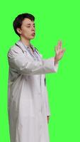 Side view Woman physician raising palm and doing stop sign in studio, expressing rejection and denial against greenscreen backdrop. General practitioner showing warning symbol with negative reaction. Camera B. video