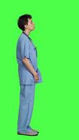 Profile Displeased nurse saying no and sighing against greenscreen backdrop, acting disappointed while she wears blue scrubs. Medical assistant with expertise shows negative gesture, being tired. Camera A. video