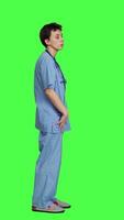 Profile Stressed nurse checking time on watch and waiting for patient to arrive at checkup examination, being impatient against greenscreen backdrop. Medical assistant with scrubs and stethoscope. Camera A. video