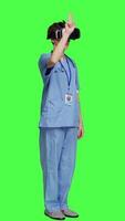 Seite Aussicht Gesundheit Spezialist mit vr Headset zu untersuchen geduldig Diagnose, steht gegen grüner Bildschirm Hintergrund. Krankenschwester funktioniert mit künstlich Intelligenz virtuell Wirklichkeit Gläser, drei dimensional. Kamera a. video