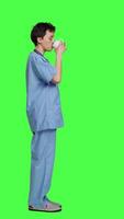 Profile Medical assistant drinking cup of coffee before starting exam appointments in the morning, enjoying caffeine refreshment against greenscreen backdrop. Nurse drinks beverage. Camera A. video