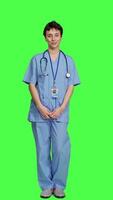 Front view Portrait of medical assistant smiling and posing with confidence, standing against greenscreen backdrop. Nurse wears blue scrubs and stethoscope, feeling successful with health expertise. Camera A. video