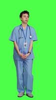 Front view Stressed nurse checking time on watch and waiting for patient to arrive at checkup examination, being impatient against greenscreen backdrop. Medical assistant with scrubs and stethoscope. Camera A. video