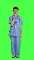 Front view Medical assistant asking to keep quiet and be silent against greenscreen, showing hush mute symbol to keep privacy and silence. Young nurse showing secrecy taboo sign. Camera A. video