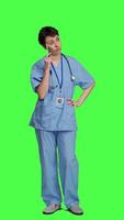 Front view Medical assistant thinking about new treatment ideas in studio, acting thoughtful while she stands against greenscreen backdrop. Pensive young nurse contemplating about healthcare ideas. Camera A. video