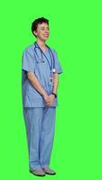 Side view Joyful medical assistant greeting patients with a smile and waving, saying hello in studio against greenscreen backdrop. Smiling cheerful nurse welcoming people at healthcare clinic. Camera A. video