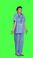 Side view Medical assistant shrugging and doing i dont know sign in studio, acting clueless and uncertain against greenscreen backdrop. Nurse in scrubs gesticulating doubtful reaction, unsure girl. Camera B. video