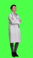 Side view Portrait of successful physician standing with arms crossed against greenscreen backdrop, wearing a white coat and stethoscope. Doctor feeling confident with healthcare expertise. Camera A. video