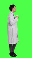 Profile Happy medic serving hot coffee cup as refreshment against greenscreen backdrop, wearing white coat and drinking caffeine beverage. General practitioner enjoying drink, medical expertise. Camera A. video