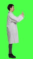 Profile Cheerful medic doing thumbs up symbol against greenscreen backdrop, expresses positivity with like sign. General practitioner with coat giving approval and being satisfied with success. Camera B. video