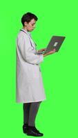 Profile Confident physician searching for new medicaments to treat disease, using laptop to browse on online web pages against greenscreen backdrop. Medic in white coat checks internet sites. Camera A. video