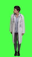 Front view General practitioner feeling impatient waiting for patients at clinic, standing against greenscreen backdrop. Young physician with white coat looking around for people, medical exam. Camera A. video