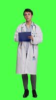 Front view Physician taking notes after patient examination against greenscreen backdrop, writing down medicaments to cure illness. Doctor in white coat using clipboard papers for checkup. Camera A. video