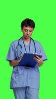 Front view Confident hospital nurse taking notes for the next medic appointment, standing over greenscreen backdrop. Medical assistant with uniform writing patient information on clipboard papers. Camera B. video