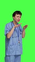 Side view Medical assistant asking to keep quiet and be silent against greenscreen, showing hush mute symbol to keep privacy and silence. Young nurse showing secrecy taboo sign. Camera B. video