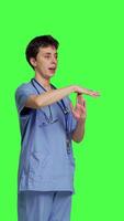 Side view Medical assistant giving timeout symbol against greenscreen backdrop, showing limits and asking for a break. Nurse doing pause or stop gesture while she wears blue scrubs. Camera B. video