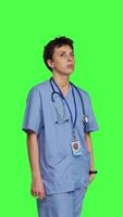 Side view Stressed nurse checking time on watch and waiting for patient to arrive at checkup examination, being impatient against greenscreen backdrop. Medical assistant with scrubs and stethoscope. Camera B. video