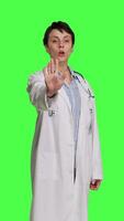 Front view Woman physician raising palm and doing stop sign in studio, expressing rejection and denial against greenscreen backdrop. General practitioner showing warning symbol with negative reaction. Camera B. video