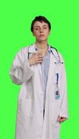 Front view Happy medic serving hot coffee cup as refreshment against greenscreen backdrop, wearing white coat and drinking caffeine beverage. General practitioner enjoying drink, medical expertise. Camera B. video