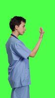 Profile Medical assistant asking a person to come over closer against greenscreen backdrop, inviting patient to approach. Nurse in scrubs calling someone at checkup examination, young surgeon. Camera B. video