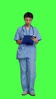 Front view Confident hospital nurse taking notes for the next medic appointment, standing over greenscreen backdrop. Medical assistant with uniform writing patient information on clipboard papers. Camera A. video