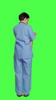 Back view Stressed nurse being in a hurry with the checkup appointments, waiting for patients to arrive at examinations. Medical assistant with scrubs acting impatient against greenscreen backdrop. Camera A. video