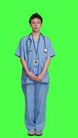 främre se ung sjuksköterska med medicinsk expertis poser med förtroende, bär blå scrubs enhetlig och leende mot grönskärm bakgrund. hälsa assistent ger Stöd till doktorer som yrke. kamera a. video