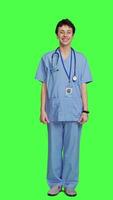 Front view Joyful medical assistant greeting patients with a smile and waving, saying hello in studio against greenscreen backdrop. Smiling cheerful nurse welcoming people at healthcare clinic. Camera A. video