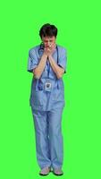 Front view Medical assistant feeling extremely sleepy against greenscreen backdrop, being overworked after the night shift. Woman nurse yawns and feels exhausted in studio, burnout and anxiety. Camera A. video