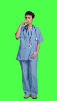 Front view Healthcare specialist enjoying hot coffee cup against greenscreen backdrop, drinking caffeine refreshment in blue scrubs. Medical assistant serving beverage at work, friendly staff. Camera A. video