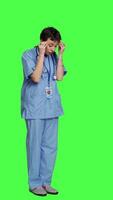 Side view Stressed furious nurse screaming at someone against greenscreen backdrop, showing rage and anger in studio. Aggressive upset medical assistant shouting and being dissatisfied. Camera A. video