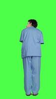 Back view Medical assistant being impatient against greenscreen backdrop, looking around and waiting for patients at consultations. Nurse with health expertise feeling frustrated while she waits. Camera A. video