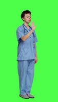 Side view Health specialist with blue scrubs showing stop sign in studio, standing against greenscreen backdrop. Nurse expressing denial and refusal with warning forbidden symbol, denying something. Camera A. video
