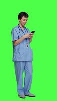 Side view Health specialist using smartphone to make important calls, standing against greenscreen backdrop. Nurse talking to patients for checkup exams on telephone line, calling people to confirm. Camera A. video