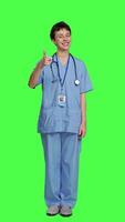 Front view Cheerful nurse giving thumbs up sign against greenscreen backdrop, showing positive gesture with a like. Medical assistant shows her approval, recommending something and being satisfied. Camera A. video