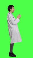 Profile Portrait of general practitioner laughing at something against greenscreen backdrop, feeling joyful and confident with her healthcare expertise. Woman medic in white coat smiling in studio. Camera A. video