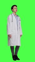 Side view Portrait of health specialist wearing a white hospital coat in studio, standing against greenscreen backdrop. Successful doctor posing with confidence, medical industry expertise. Camera A. video