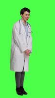 Side view Portrait of general practitioner laughing at something against greenscreen backdrop, feeling joyful and confident with her healthcare expertise. Woman medic in white coat smiling in studio. Camera A. video