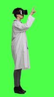 Profile Physician consulting patients with virtual reality futuristic glasses, wears white coat against greenscreen backdrop. General practitioner uses artificial intelligence interactive headset. Camera A. video