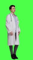 Side view Portrait of physician wearing a white coat and a stethoscope for exams, standing against greenscreen backdrop. Doctor specialist working in healthcare industry, medical expertise. Camera A. video