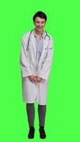 Front view Portrait of general practitioner laughing at something against greenscreen backdrop, feeling joyful and confident with her healthcare expertise. Woman medic in white coat smiling in studio. Camera A. video