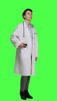 Side view Woman physician looking around for patients to come at checkup exams, waiting for someone standing against greenscreen backdrop. General practitioner with white coat feeling impatient. Camera A. video