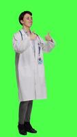 Side view Cheerful medic doing thumbs up symbol against greenscreen backdrop, expresses positivity with like sign. General practitioner with coat giving approval and being satisfied with success. Camera B. video