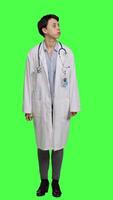 Front view Woman physician looking around for patients to come at checkup exams, waiting for someone standing against greenscreen backdrop. General practitioner with white coat feeling impatient. Camera A. video