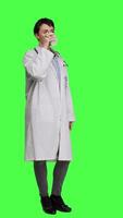 Side view Woman physician drinking a cup of coffee against greenscreen backdrop, taking a break from medical work. Specialist serving caffeine refreshment in studio, wearing a white coat. Camera A. video