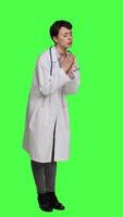 Side view Hopeful physician holding hands in a prayer sign against greenscreen backdrop, asking for peace and forgiveness in studio. Woman medic specialist in white coat does meditation. Camera A. video