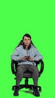 Front view Woman gamer playing online video games with controller, sitting in an office chair against greenscreen backdrop. Joyful person having fun with e sport competition, modern gaming setup. Camera A.